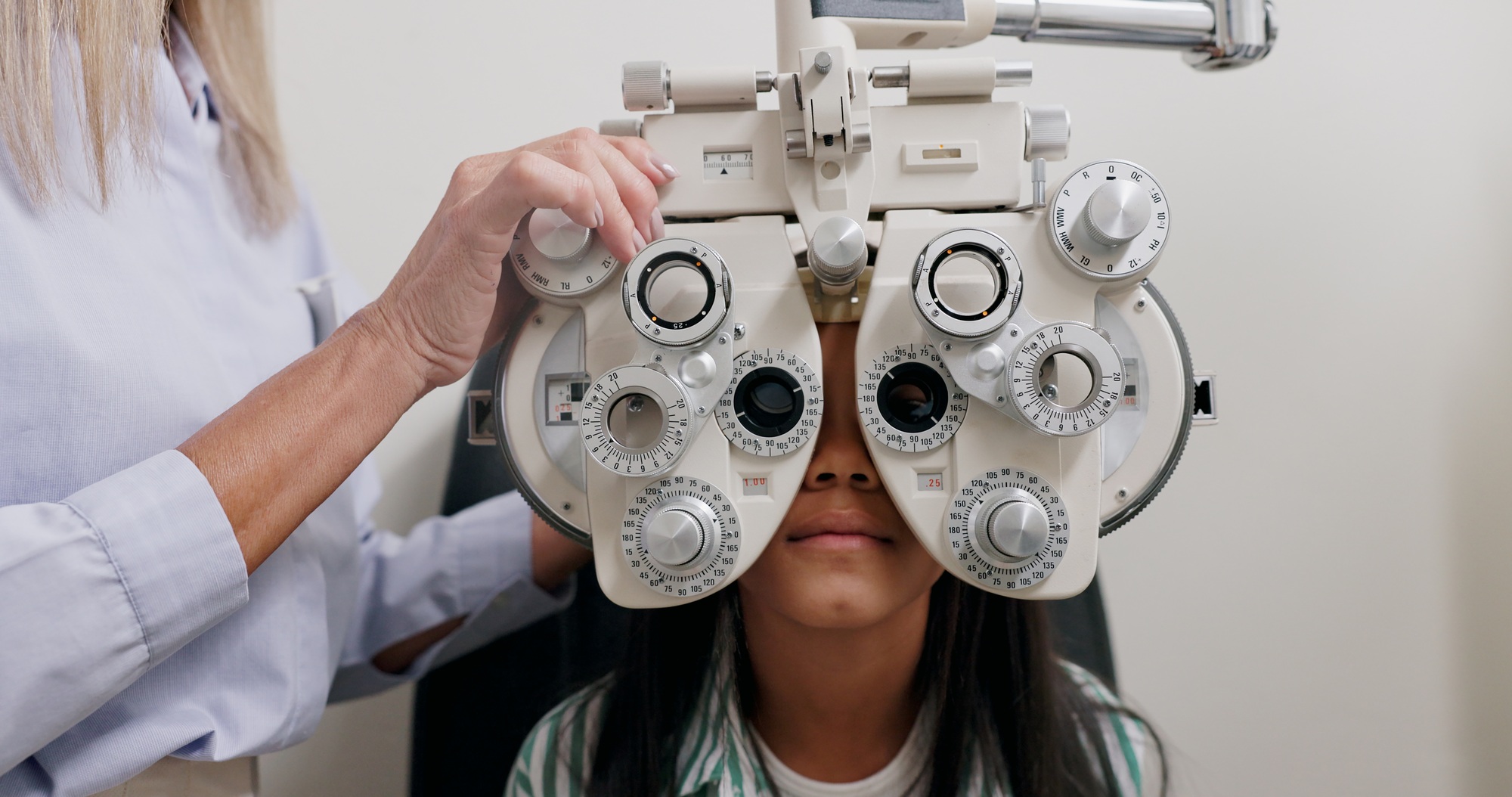 Eye care, vision and child in clinic, test and hand of specialist, phoropter or refractor for girl.